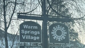 Señal direccional que indica 'Warm Springs Village' y 'Restaurantes/tiendas' a la izquierda, y 'Estacionamiento para esquiadores' a la derecha.