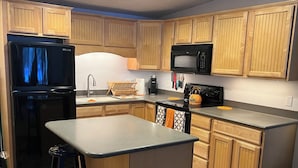 Una cocina compacta con armarios de madera, un refrigerador negro, un microondas y una estufa.