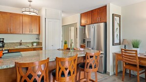 A modern kitchen with wooden cabinets, a stainless steel refrigerator, and a granite countertop. - Lush 1BD garden view, Steps from Beach & Pool - Maui Vista 1106 (Kihei)