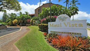 A sign for 'Maui Vista' with a clear road and lush landscaping. - Lush 1BD garden view, Steps from Beach & Pool - Maui Vista 1106 (Kihei)