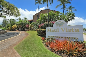 Señal de 'Maui Vista', con un césped cuidado y plantas tropicales.