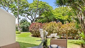 A round table with a white bowl, a glass, and a vase with white flowers. - Lush 1BD garden view, Steps from Beach & Pool - Maui Vista 1106 (Kihei)