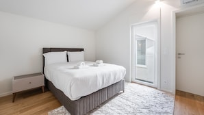 A modern bedroom with a bed, bedside table, and a door leading to a balcony.