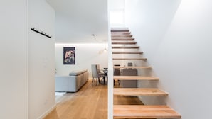 A modern interior with a wooden staircase, a sofa, a dining table, and a poster on the wall.