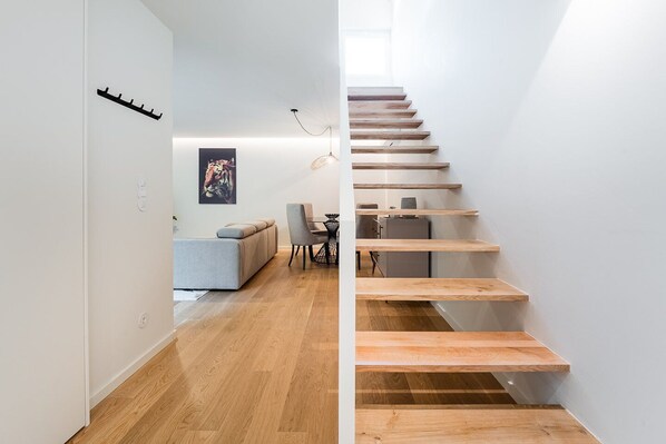 A modern interior with a wooden staircase, a sofa, a dining table, and a poster on the wall.