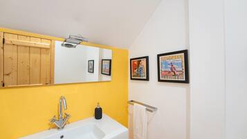 Une salle de bain avec un lavabo blanc, des murs jaunes, un panneau en bois, un miroir et deux tableaux encadrés.