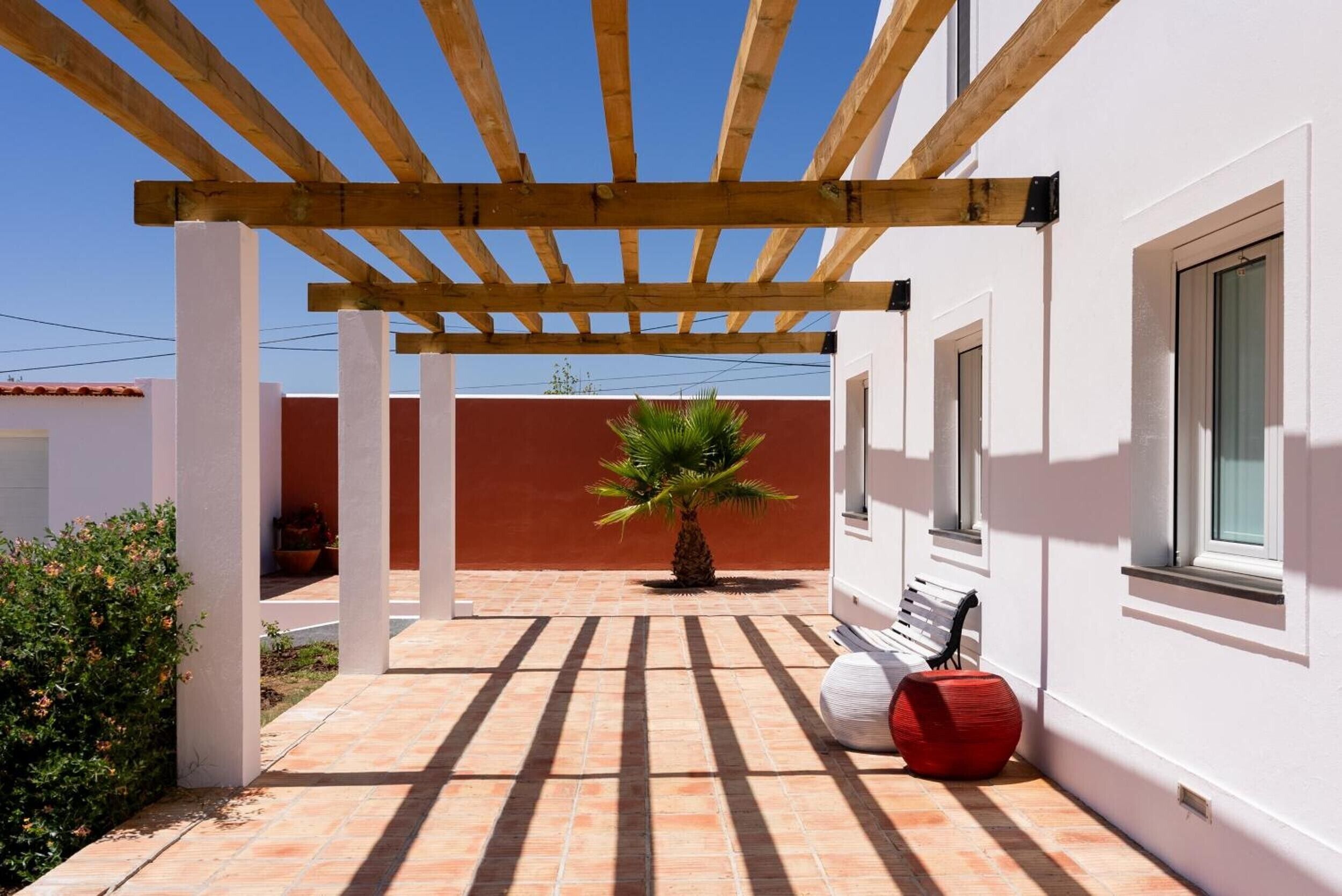 A covered outdoor area with a wooden pergola, a palm tree, and a red spherical object.