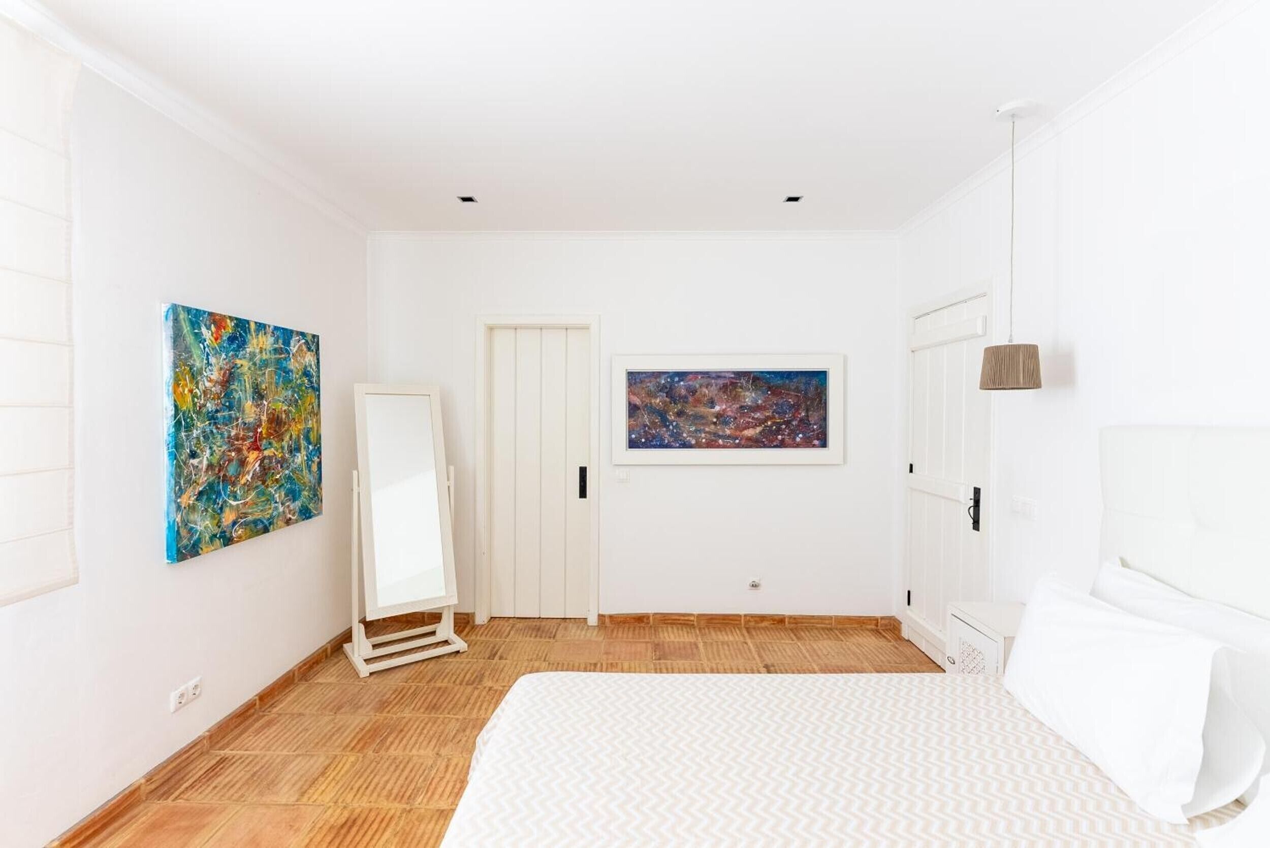 Une chambre à coucher avec un lit, une porte blanche, un tableau encadré et un grand miroir.