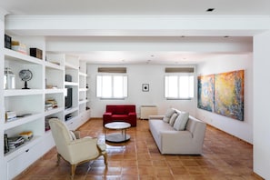 Un vaste espace de vie comprenant un canapé rouge, un canapé beige, une table basse ronde et une bibliothèque blanche remplie de livres et d’objets décoratifs.
