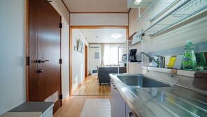 A narrow kitchen with a wooden door, a white refrigerator, a stainless steel sink, and a coffee maker. - YADOKITO 1 201 (Otaru)
