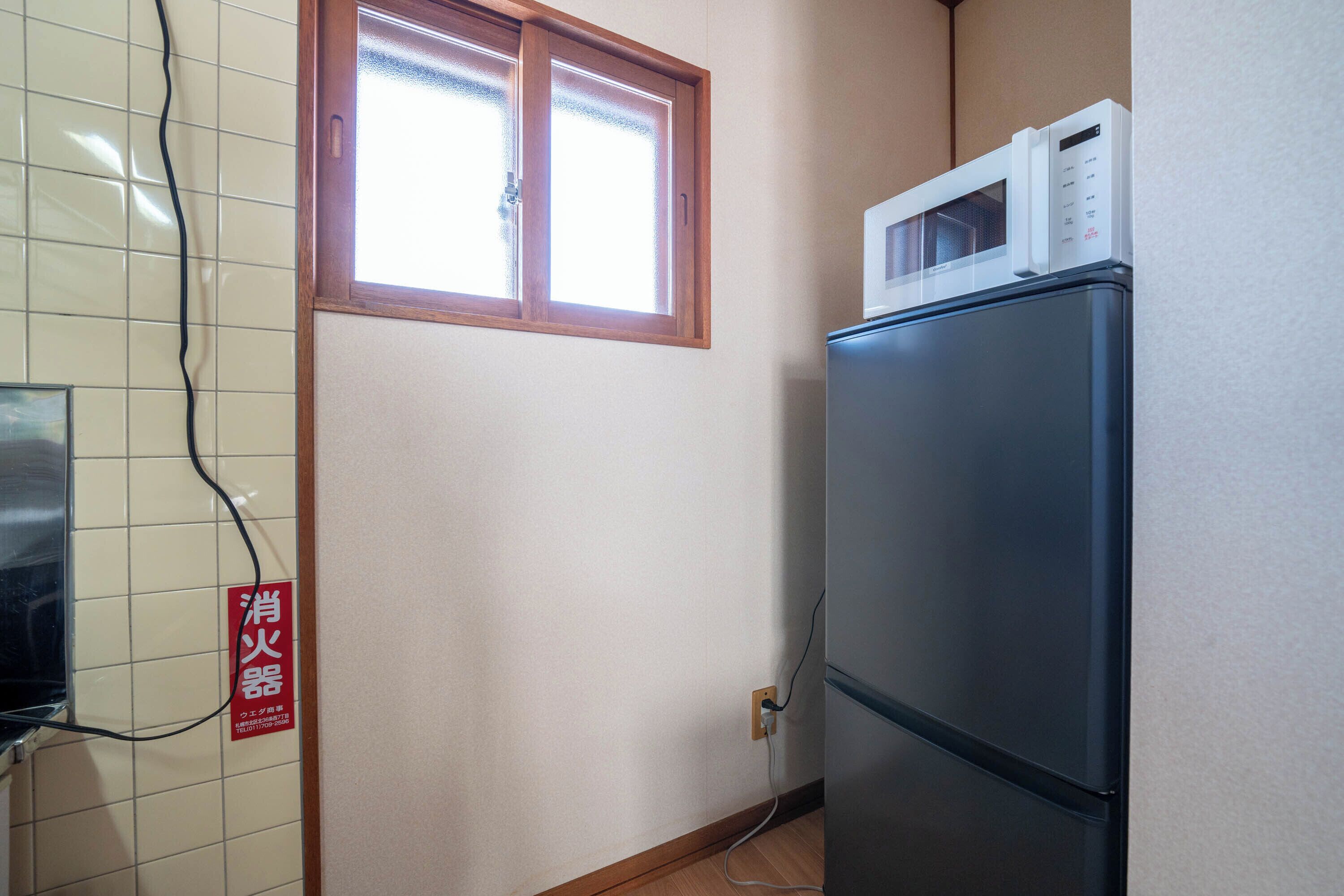 Una cocina con refrigerador, microondas encima, ventana y un cartel en la pared.