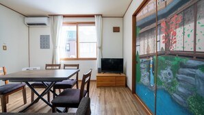 A room with a wooden dining table, chairs, a flat-screen TV, and a traditional Japanese sliding door with a nature scene. - YADOKITO 1 201 (Otaru)