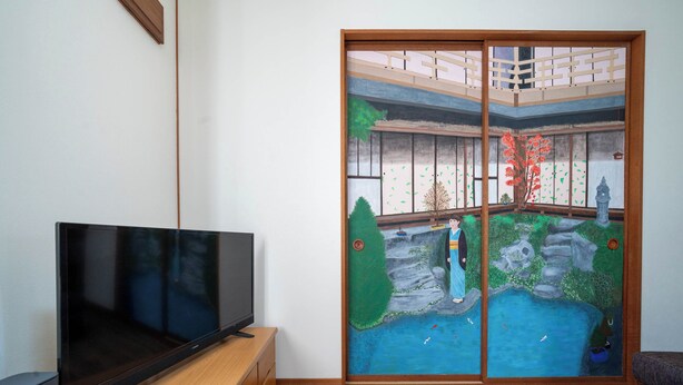 A room with a flat-screen TV on a wooden stand, a sliding door with a traditional Japanese garden mural, and a wooden floor. - YADOKITO 1 201 (Otaru)