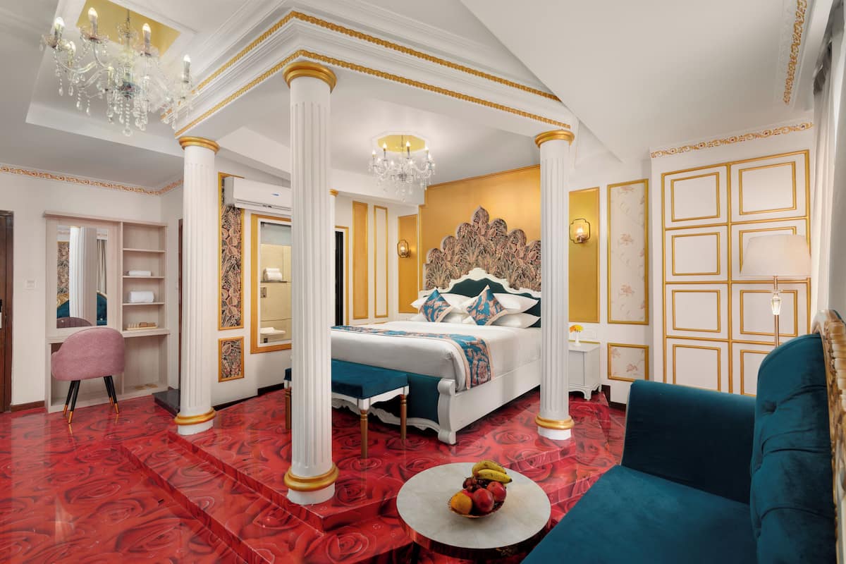 Un dormitorio lujoso con cama con dosel, una zona de estar con sofá azul y una alfombra roja estampada.