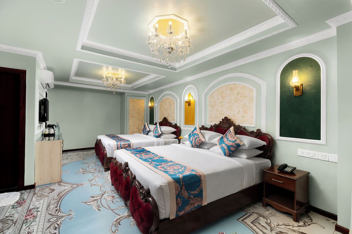Habitación de hotel con una cama grande, dos mesitas de noche, una araña y una alfombra con motivos florales.