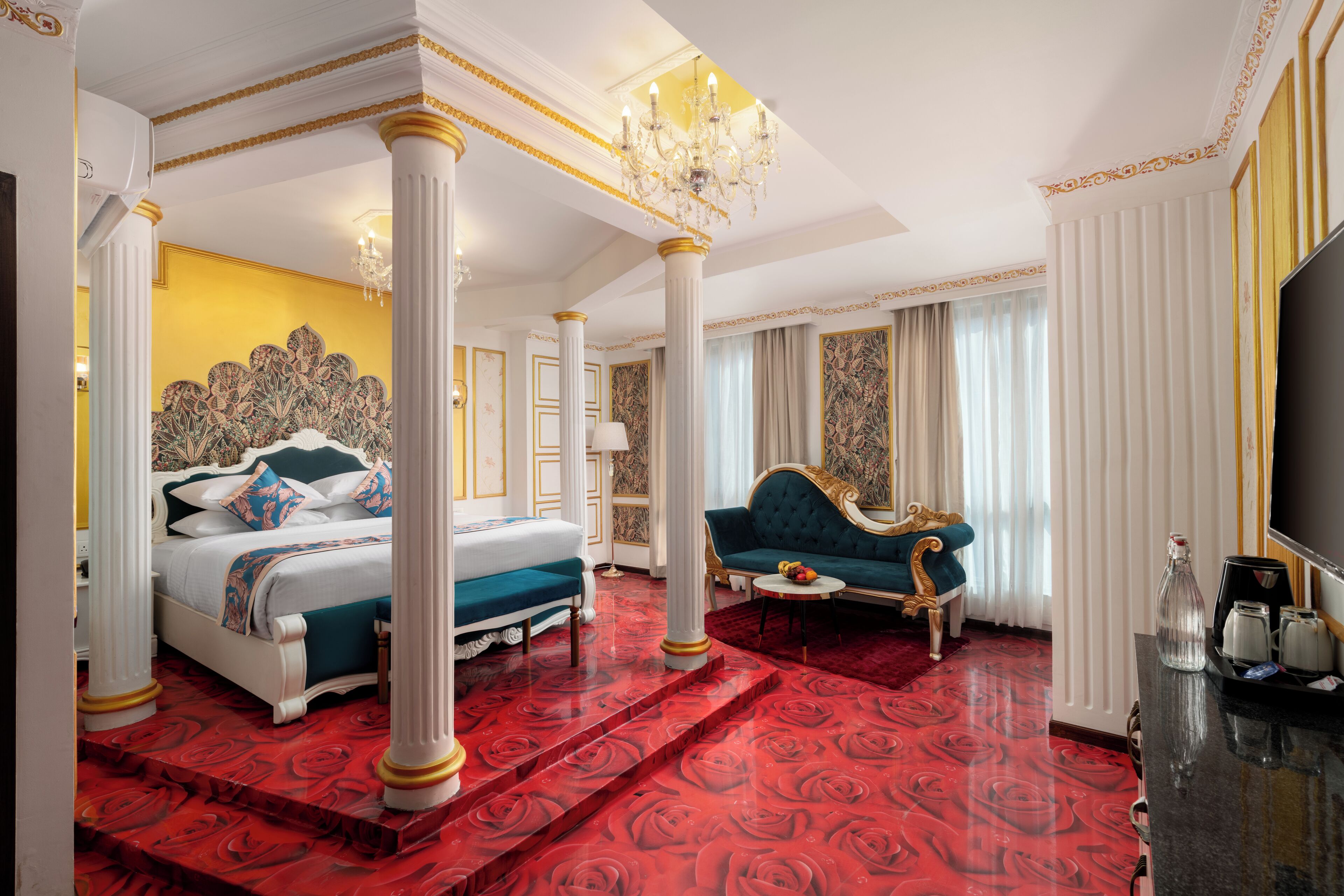 A luxurious bedroom with a four-poster bed, a sitting area with a sofa, and a television on a dresser.