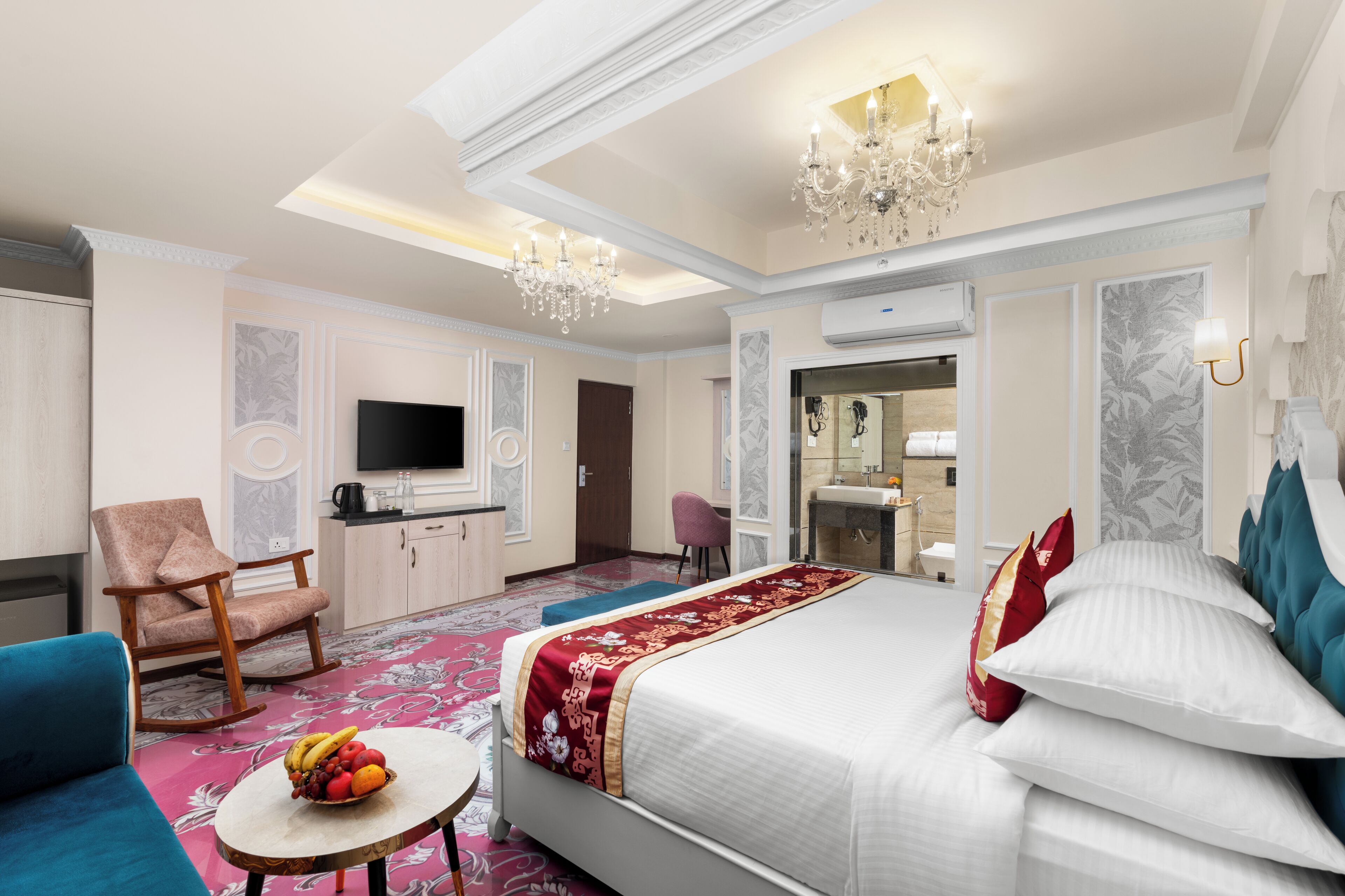 Une chambre d’hôtel avec un grand lit, une télévision, un bureau, une chaise et un panier de fruits.