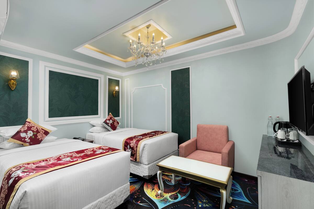 Habitación de hotel con dos camas, una silla, una mesita, televisión y cafetera.