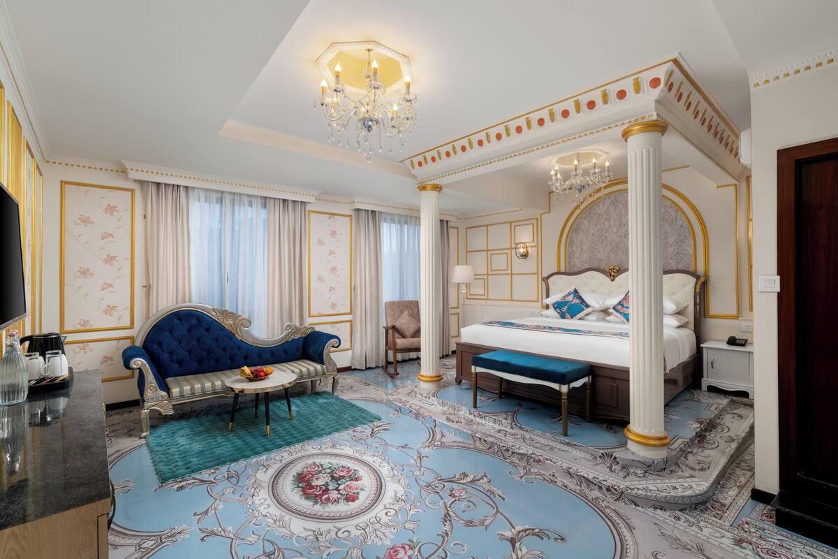 Un dormitorio lujoso con cama con dosel, un sofá azul, una mesita con fruta y un candelabro.