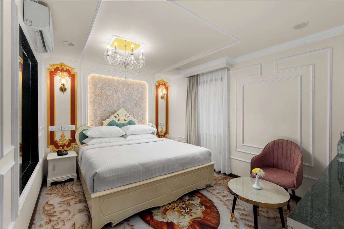 Una habitación de hotel con una cama grande, una mesa redonda con un florero, una silla y una araña.
