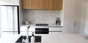 A modern kitchen with white cabinetry, a herringbone tile backsplash, and a black countertop. - Peace in Paradise (Taupō)