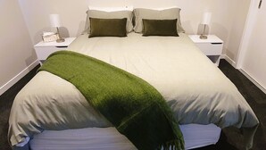 En pænt redt seng med et grønt tæppe, hvide sengetæger og to sengeborde med lamper.