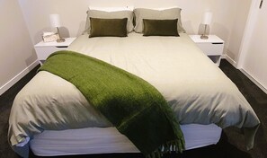 A neatly made bed with a green throw blanket, white bedding, and two bedside lamps on white nightstands. - Peace in Paradise (Taupō)