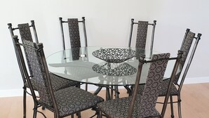 Et rundt glasbord med et mønstret metalstel, omgivet af seks stole med mønstret betræk.