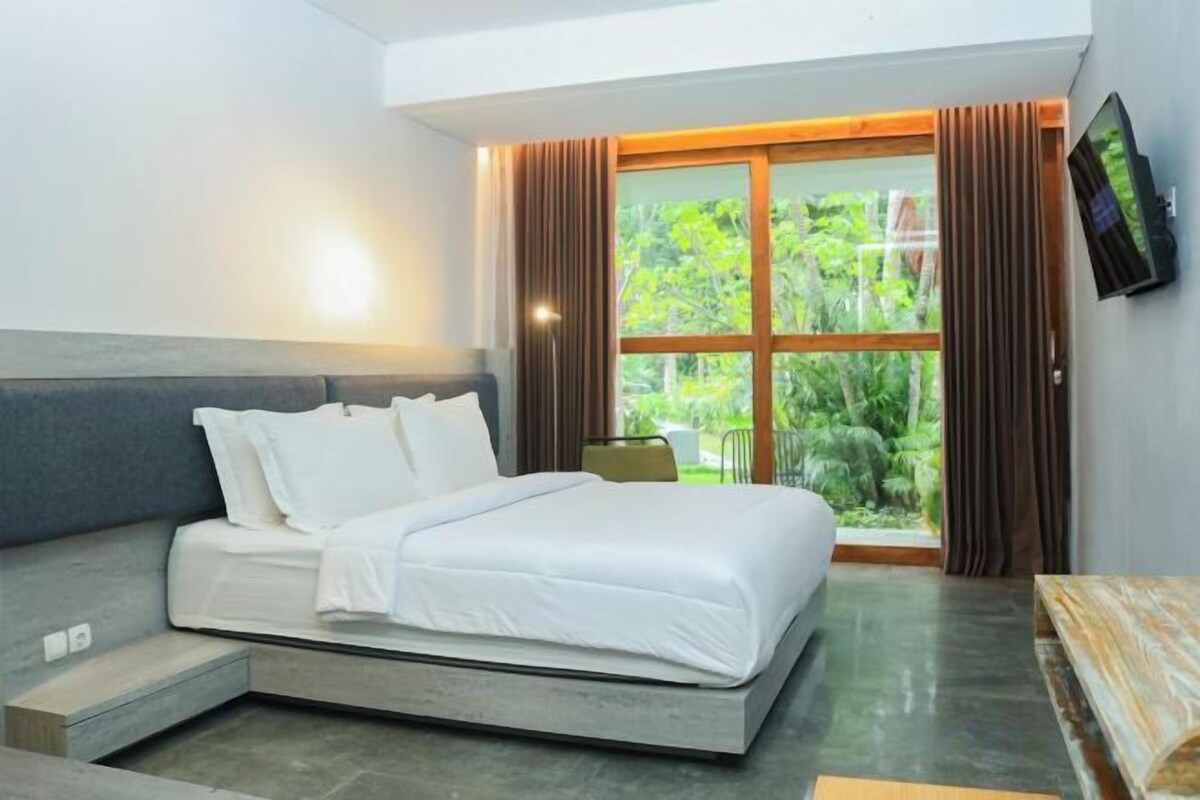 A modern hotel room with a bed, a TV, and a large window with curtains.