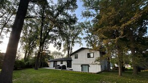A single-story house with a covered patio area, surrounded by trees and a grassy yard.