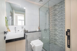 A modern bathroom with a glass shower enclosure, a white sink, and a toilet. - Skyline Views Binghatti Avenue (Dubai)