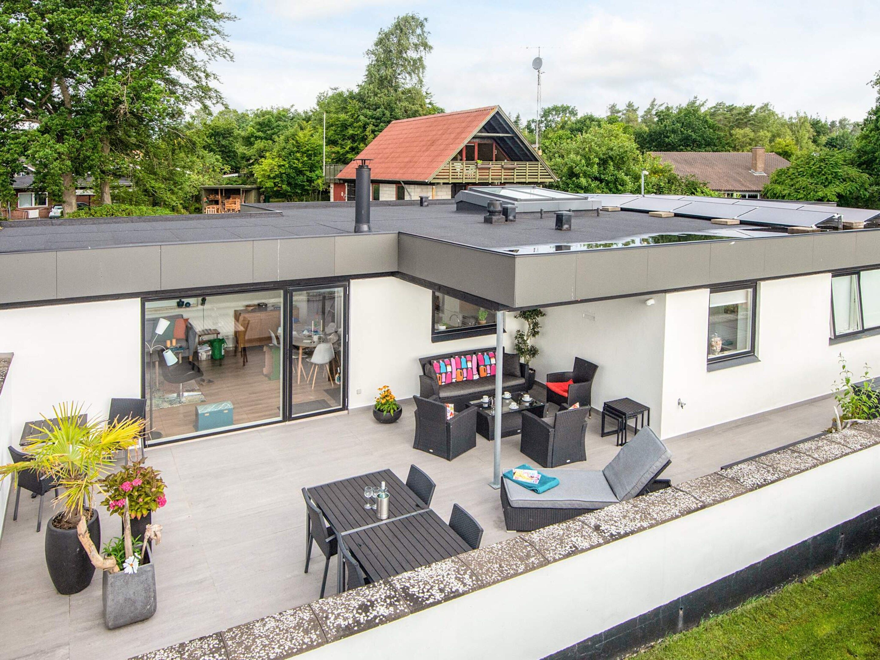 Una casa moderna con techo plano, un patio con mobiliario exterior y un garaje visible.
