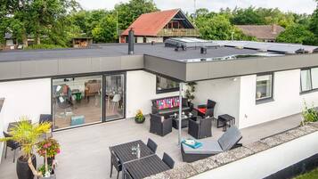 Una casa moderna con techo plano, un patio con mobiliario exterior y un garaje visible.