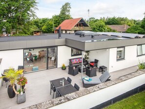Una casa moderna con techo plano, un patio con mobiliario exterior y un garaje visible.
