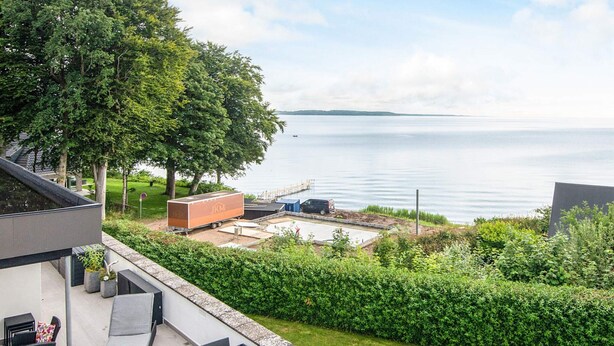 A modern outdoor patio with a dining area, a lounge chair, and a view of a lake. - 5 Star Holiday Home in Borkop (Borkop)