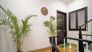 A hallway with two potted plants, a wooden door, and a staircase with green railings. - Footprint Hostel Udaipur (Udaipur)