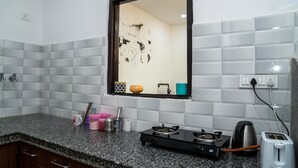 A kitchen with a gas stove, a toaster, and a kettle. There is a window with a mirror reflecting the room. - Footprint Hostel Udaipur (Udaipur)