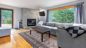 Un salon moderne avec une cheminée en pierre, un canapé gris, une table basse en bois et un tapis à motifs.