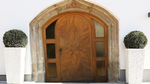 A wooden arched door with a decorative pattern, flanked by two potted topiaries. - Apartment with shared wellness and fitness (Piesendorf)