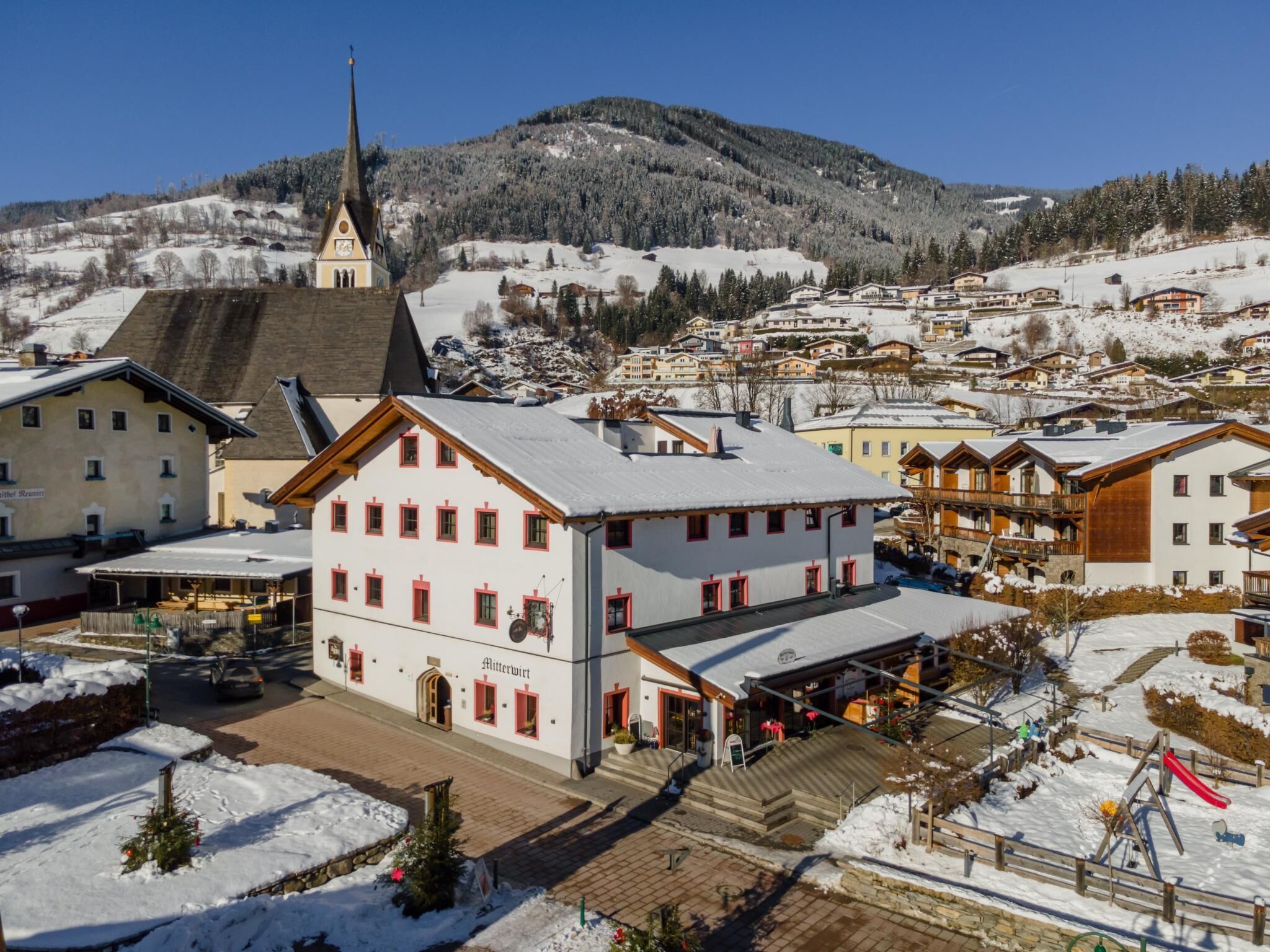 Un pueblo cubierto de nieve con arquitectura alpina tradicional, que incluye una iglesia y varias edificaciones residenciales.