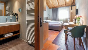 A modern hotel room with a wooden ceiling, a large bed, a bathroom with a sink and mirror, and a dining area with a table and chairs. - Apartment with shared wellness and fitness (Piesendorf)