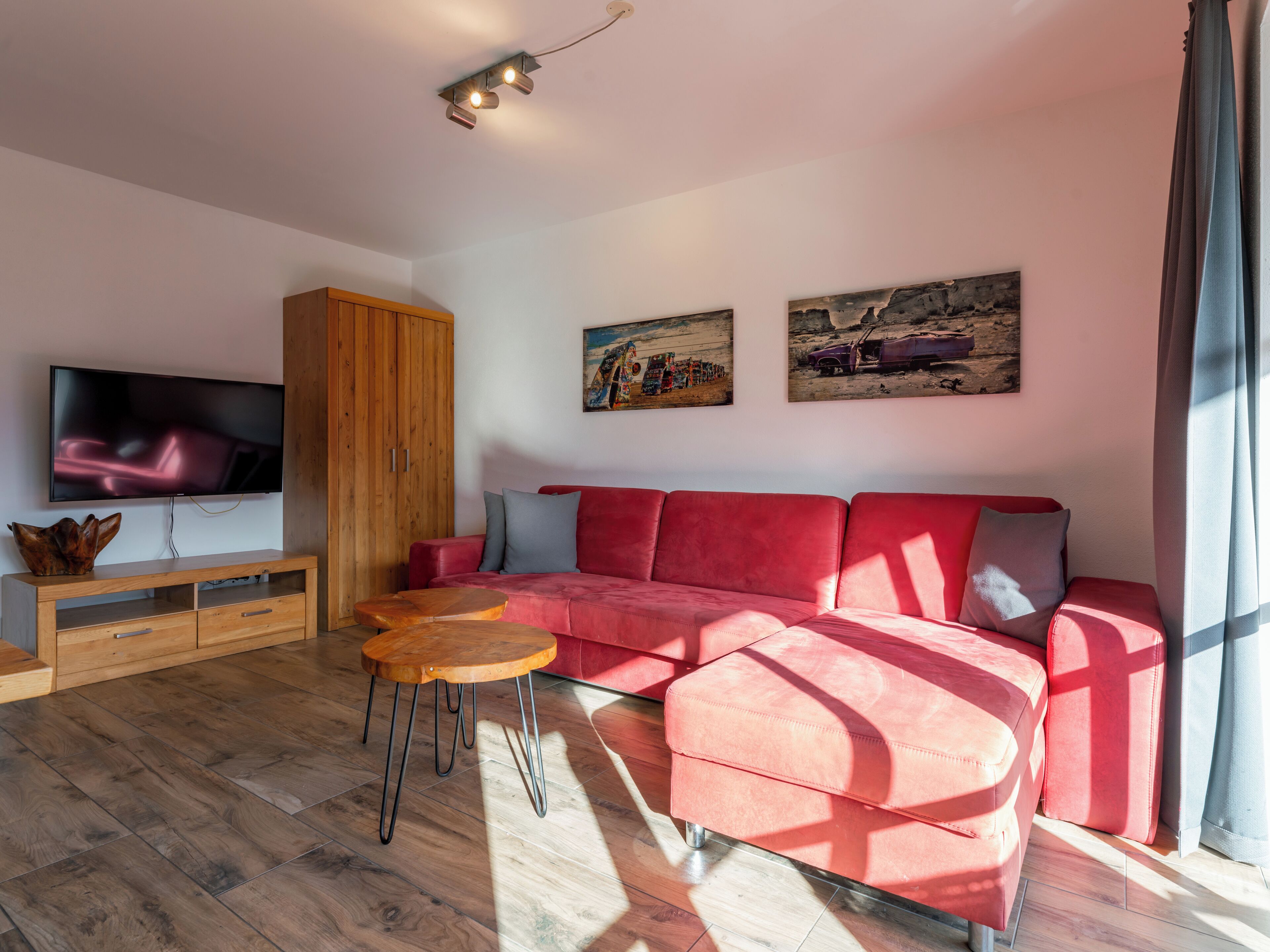 Una sala de estar moderna con un sofá seccional rojo, piso de madera, un televisor de pantalla plana y dos cuadros en la pared.
