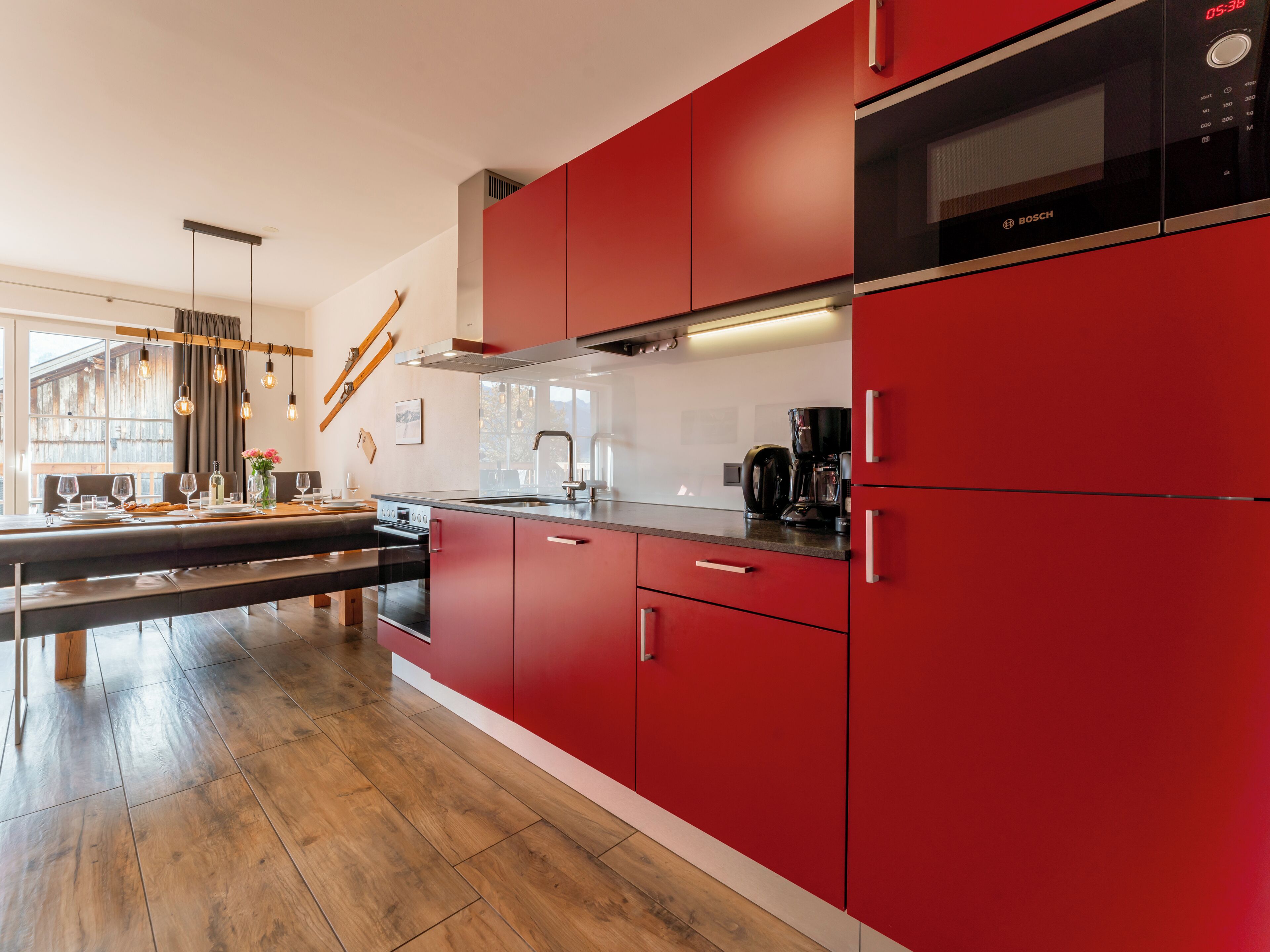 Une cuisine moderne avec des meubles rouges, un four à micro-ondes de la marque Bosch et un coin repas comprenant un banc et une table en bois.