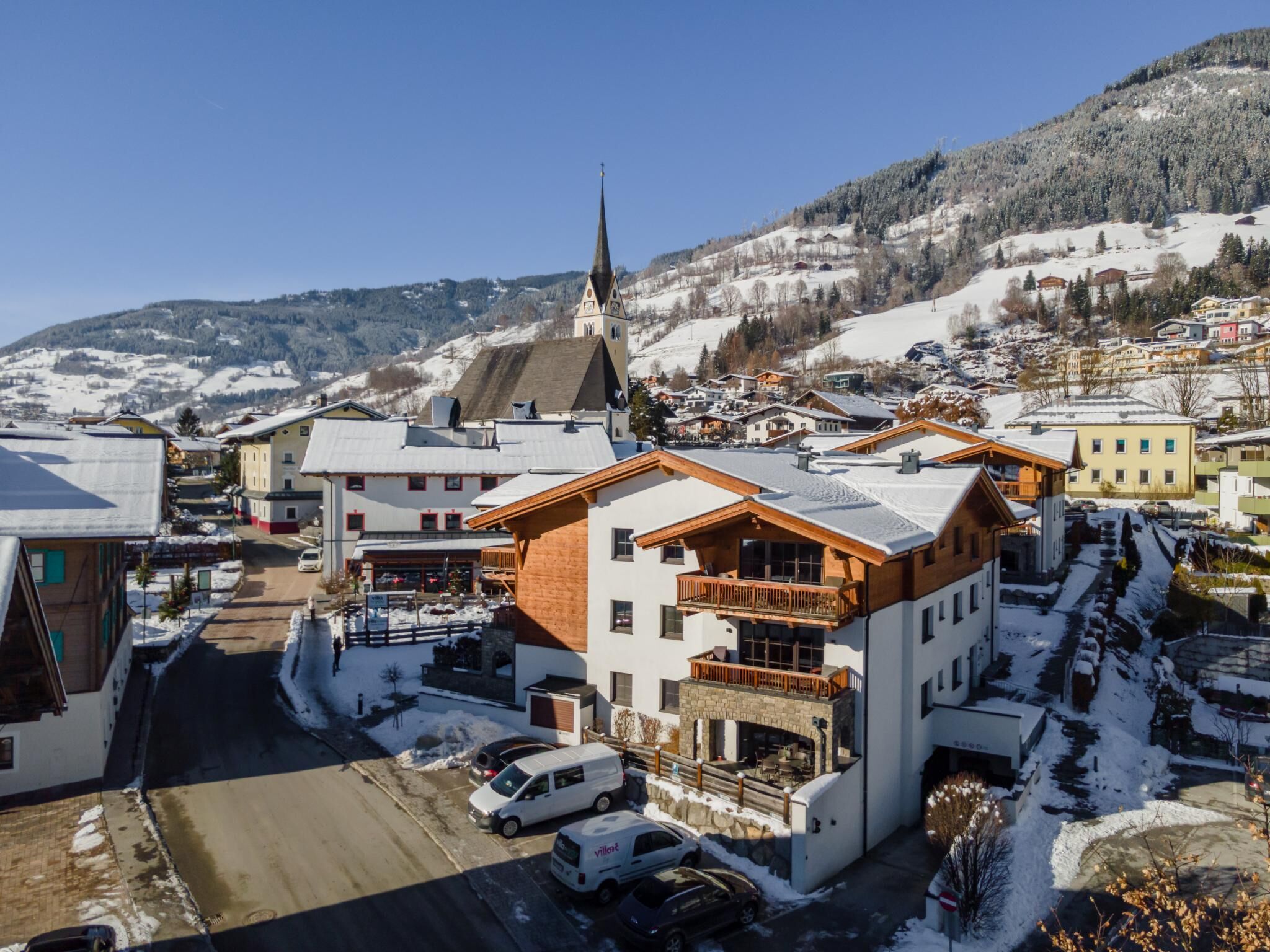 Une ville enneigée, avec un clocher d’église imposant, des bâtiments modernes et une vue dégagée sur les montagnes environnantes.