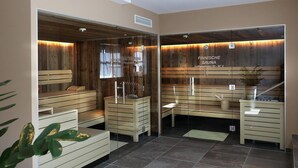 Eine Sauna mit Holzbänken und Glaswänden, ein Schild mit einer Temperaturanzeige von 90-95°C und eine Zimmerpflanze rechts.