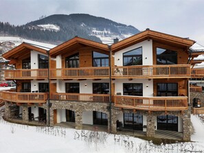 Un chalet de varios pisos con balcones de madera y cimientos de piedra, frente a un paisaje montañoso nevado.
