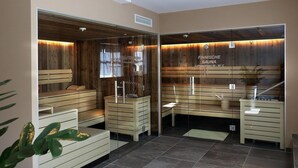 A sauna with wooden benches and glass doors, a tiled floor, and a plant in the corner.