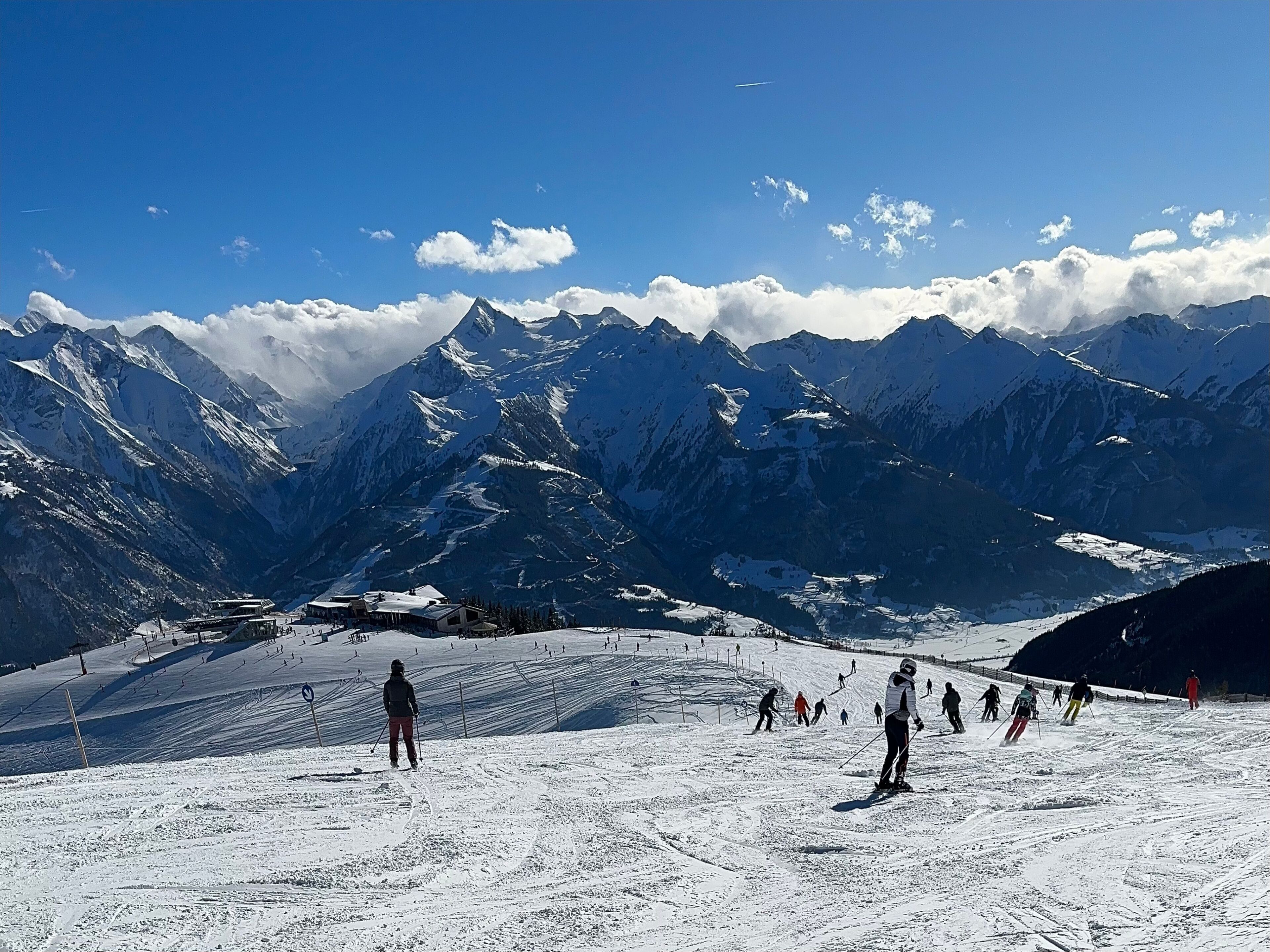 Une station de ski dotée d’un télésiège, avec des skieurs et des montagnes enneigées sous un ciel dégagé.