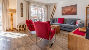 A modern living room with a grey sofa, red chairs, a wooden coffee table, and a large window with a view of buildings. - Cosy apartment with a large balcony and wellness (Piesendorf)