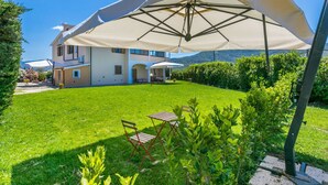 Une maison à deux étages avec une grande pelouse, du mobilier d’extérieur et une pergola surmontée d’un auvent blanc.